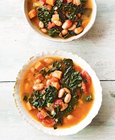 two bowls filled with soup and vegetables on top of a white wooden table next to each other