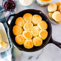 some biscuits are cooking in a skillet with butter and jams on the side