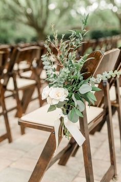 an arrangement of white flowers and greenery sits on the back of a wooden chair