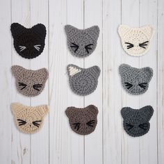 six crocheted cats are arranged on a white wooden surface, each with their eyes closed