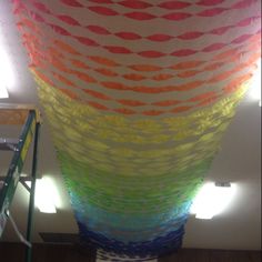 a large multicolored piece of art hanging from a ceiling in a room with ladders