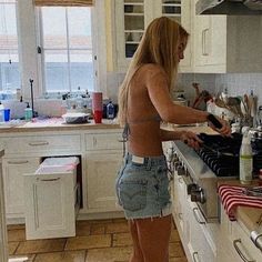 a woman standing in a kitchen preparing food on top of a stove next to an oven