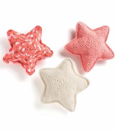 three crocheted stars are shown on a white surface, one is pink and the other is red