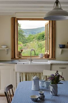 a kitchen with a sink, window and table in front of an open window looking out onto the countryside