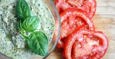 a wooden cutting board topped with sliced tomatoes and dip in a bowl next to basil leaves