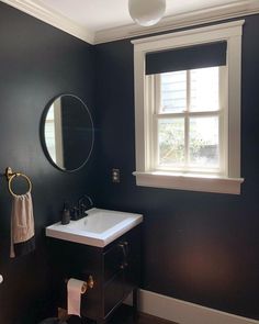 a white sink sitting under a bathroom mirror next to a window in a dark colored room