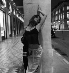 a woman leaning up against a pillar on the sidewalk