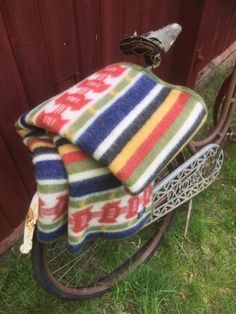 A Rattvik blanket, made from 100% Norwegian wool and designed by Kerstin Landström, is draped over the back of a vintage bicycle parked on grass near a red wooden wall, highlighting Swedish cultural heritage. Viking Books, Wool Blankets, Dala Horse, Wall Vinyl Decor, Book Clothes, Blue Blanket, Seat Pads, Cultural Heritage, Gift Store