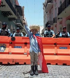 a young boy dressed as a mexican standing in front of orange barricades with police behind him