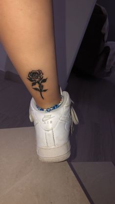 a woman's foot with a rose tattoo on her left leg and a blue beaded bracelet around the ankle