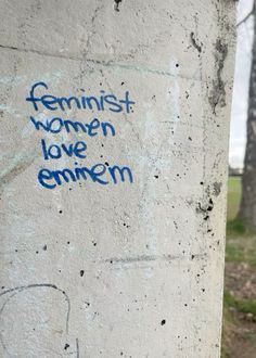 graffiti written on the side of a cement pillar in front of some trees and grass