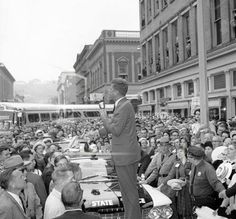 a man standing on top of a car in front of a large group of people