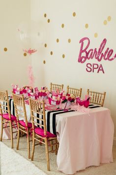 a table set up for a barbie birthday party with pink and gold decorations on the wall