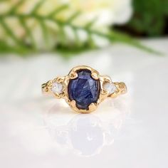 a gold ring with a blue sapphire and three white diamonds on the side, sitting on a table next to flowers