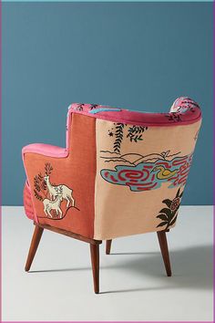 an upholstered chair with colorful designs on the back and arms, in front of a blue wall