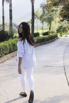 a woman in white is walking down the street with her hand on her hip and looking off to the side