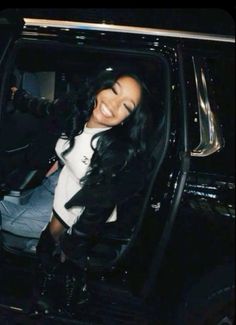 a woman sitting in the passenger seat of a black car with her hand out and smiling