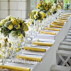 a long table with yellow napkins and white vases filled with flowers on it