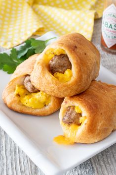 two sausage and egg breakfast rolls on a white plate with mustard in the middle, sitting next to a jar of ketchup