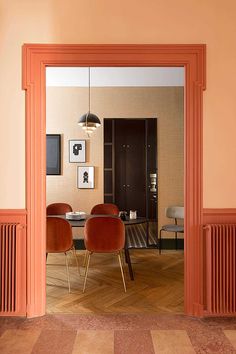 an open door leading into a dining room with orange chairs and pictures on the wall