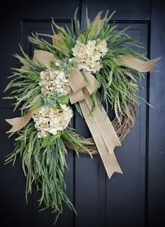 a wreath with white flowers and greenery hangs on a black front door, decorated with burlap ribbon