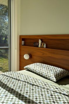 a bed with two pillows and a teddy bear on the headboard in front of a window