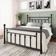 a black metal bed frame with white sheets and pillows in a green room next to two pictures on the wall