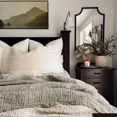 a bedroom with a bed, dresser and mirror in the corner that has a painting on the wall above it