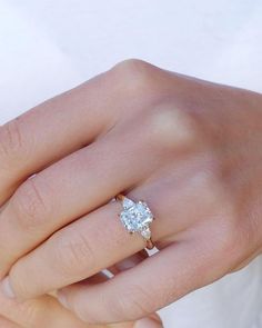 a woman's hand with a diamond ring on top of her finger and the other hand holding an engagement ring