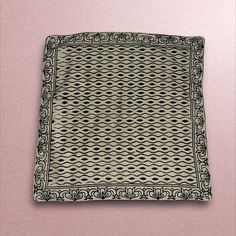 a black and white square shaped object on a pink surface with an intricate design in the middle