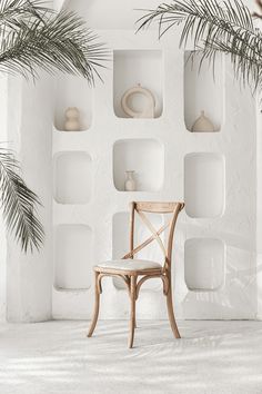 a wooden chair sitting in front of a white wall with shelves on it and plants