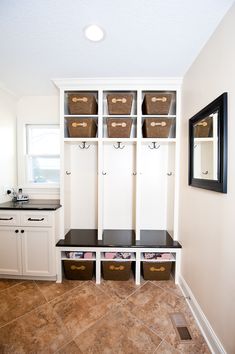 a mud room with white cabinets and brown bins