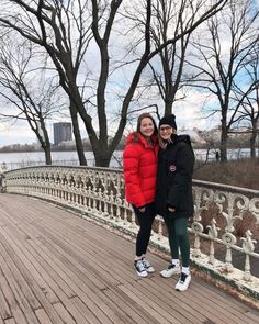 two people standing on a bridge in front of trees