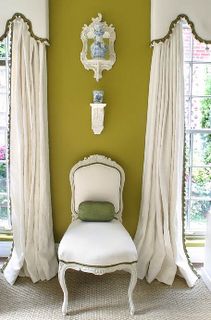 a white chair sitting in front of a window next to a wall with two windows