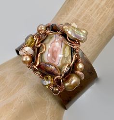 "Pink and shades of soft browns and beige....  Starting with a copper cuff bracelet that I have hammered and heated for an amazing color... I then chose the large jasper stone that is the centerpiece of this bracelet. I love the swirling shades of pink and cream.  I encased it in a freeform, forged copper bezel with a unique organic shape to it.  I have given it an artistic and organic wire wrap . For additional accents I have used beads in stone, glass and pearls to enhance the shades of the st Elegant Adjustable Brown Cuff Bracelet, Elegant Brown Cuff Bracelet As Gift, Elegant Brown Cuff Bracelet Gift, Bohemian One-of-a-kind Cuff Bracelet, Unique Bronze Wire-wrapped Bracelets, Adjustable Wire Wrapped Brown Jewelry, Unique Wire Wrapped Bronze Bracelets, Unique Bronze Wire Wrapped Bracelets, Brown Copper Cuff Bracelet As Gift