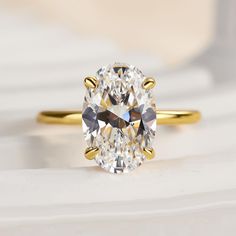 an oval cut diamond sits on top of a white surface with gold trimmings