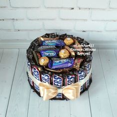 a cake decorated with chocolates and candies on a white wooden table next to a brick wall