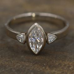 Moissanite White Gold Hand Made Vintage Inspired Engagement Ring - Marquise Ring - Triangle Engagment Ring - Alternative Engagment RingThis listing is for the moissanite ring only • This ring features a dazzling 10x5mm colorless Forever One moissanite marquise by Charles and Colvard and is flanked by two 3.5mm Forever One colorless moissanite trilliants also by Charles and Colvard. The center setting is 12x6mm in length and width. The band is 3mm in width. I include the lifetime warranty card by Promise Moissanite Marquise Wedding Ring, Timeless Marquise Cut Lab Grown Diamond Jewelry, Luxury Marquise Three-stone Jewelry, Luxury Three-stone Marquise Jewelry, Elegant Trillion Cut Ring With Bezel Setting, Trillion Cut Platinum Diamond Ring With Center Stone, Trillion Cut Moissanite White Gold Ring, Marquise Cut Lab Grown Diamond Ring With Center Stone, White Gold Moissanite Ring With Trillion Cut