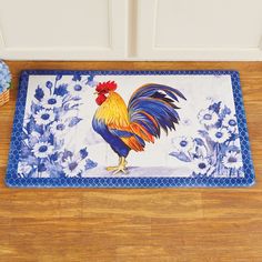 a blue and white rooster door mat on the floor next to a vase with flowers