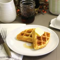 two waffles on a white plate with butter and syrup next to a fork