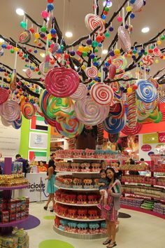 two women are standing in the middle of a store with candy decorations hanging from the ceiling