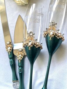 three green plastic utensils with gold decorations on them next to a white rose