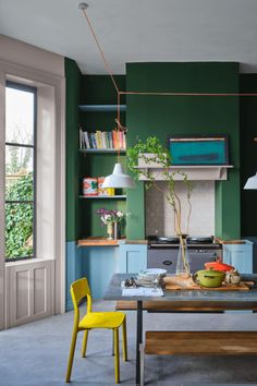 a kitchen with green walls and yellow chairs in front of the counter top, next to a wooden dining table