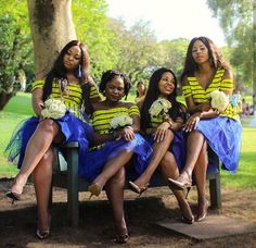 four women are sitting on a bench in the park, one is wearing a yellow and blue striped shirt