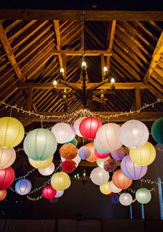 many colorful lanterns hanging from the ceiling in a room with wooden beams and lights on it