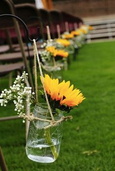 sunflowers and baby's breath are tied to mason jars in the grass