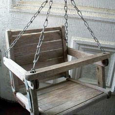 a wooden swing with chains hanging from it's sides in front of a window