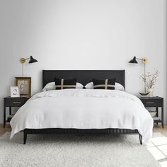 a white bed with black headboard and two lamps on either side of the bed