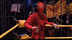 a man in a red suit and mask standing next to a barricade with people behind him