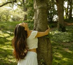 a woman leaning up against a tree in the woods